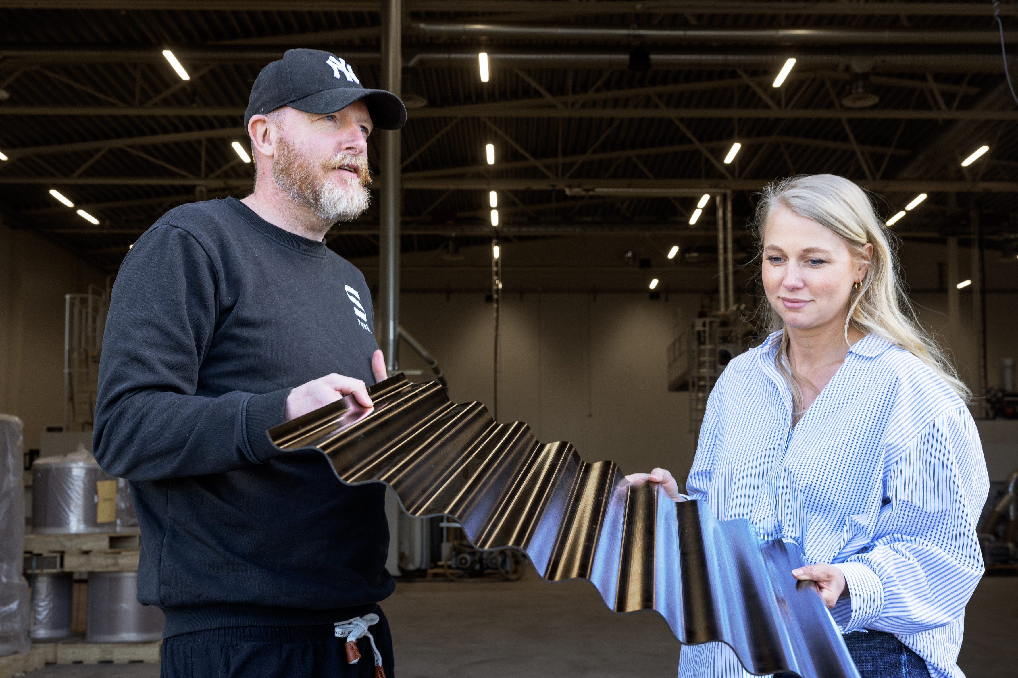 Vd Anders Breitholtz och produktionschef Hanna Adler kollar fasadplattan Sinus som är tillverkad enligt samma princip som stolen